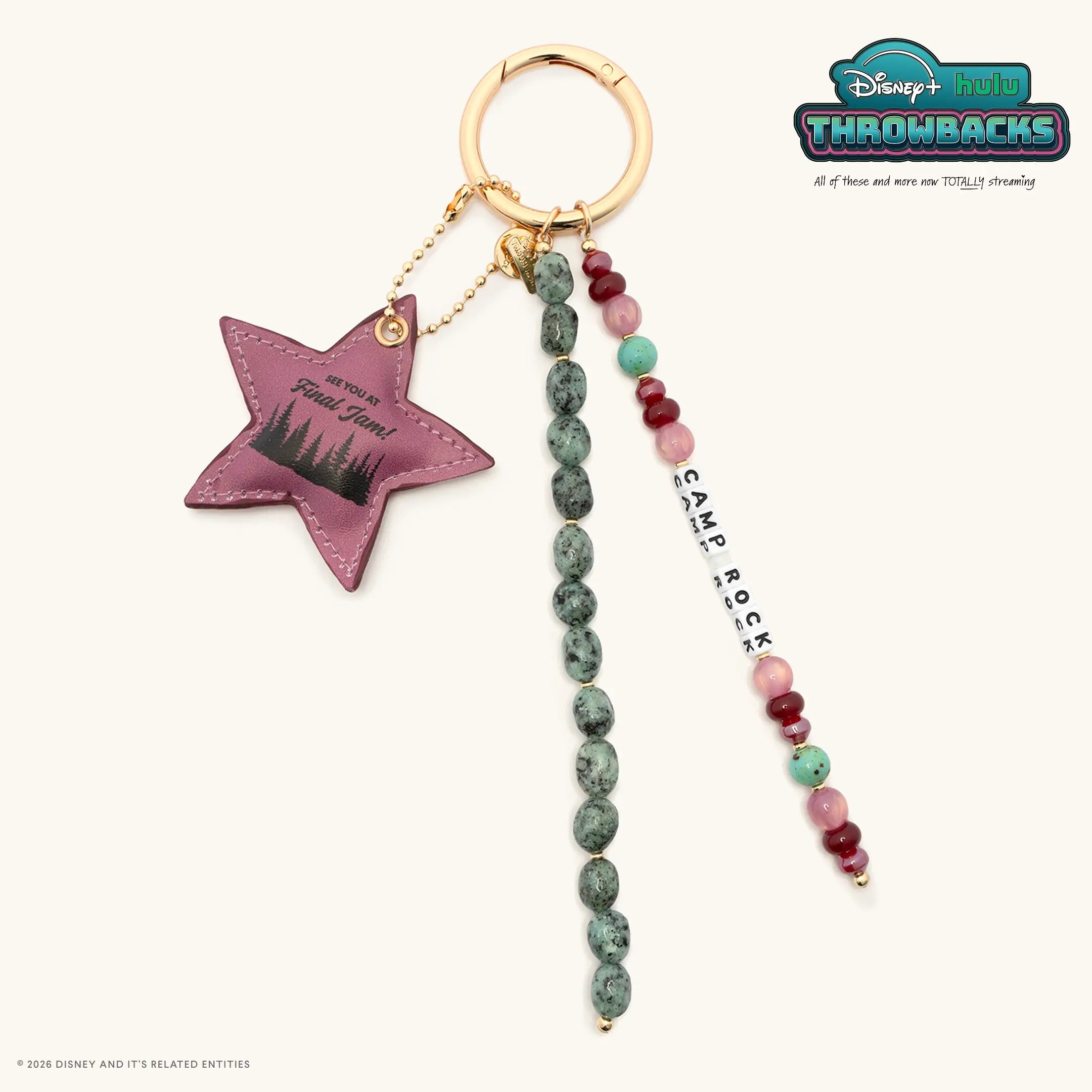 Camp Rock Disney+ Hulu Throwbacks bag charm with a gold ring, mauve faux leather star charm reading See You At Final Jam, green speckled stone beads, and Camp Rock white letter beads, flat lay on cream