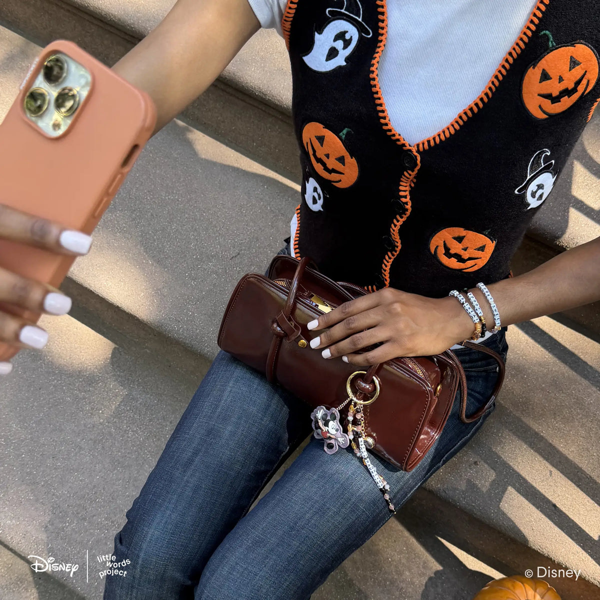 Spooky Sweet Disney's Winnie the Pooh bracelet on-model with the Spooky and Trick or Treat bracelets, Happy Haunting Bag Charm clipped to a brown handbag, Halloween sweater vest