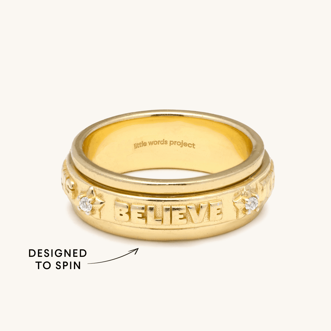 Gold "BELIEVE" spinner ring by Little Words Project, designed to spin, on a light background.