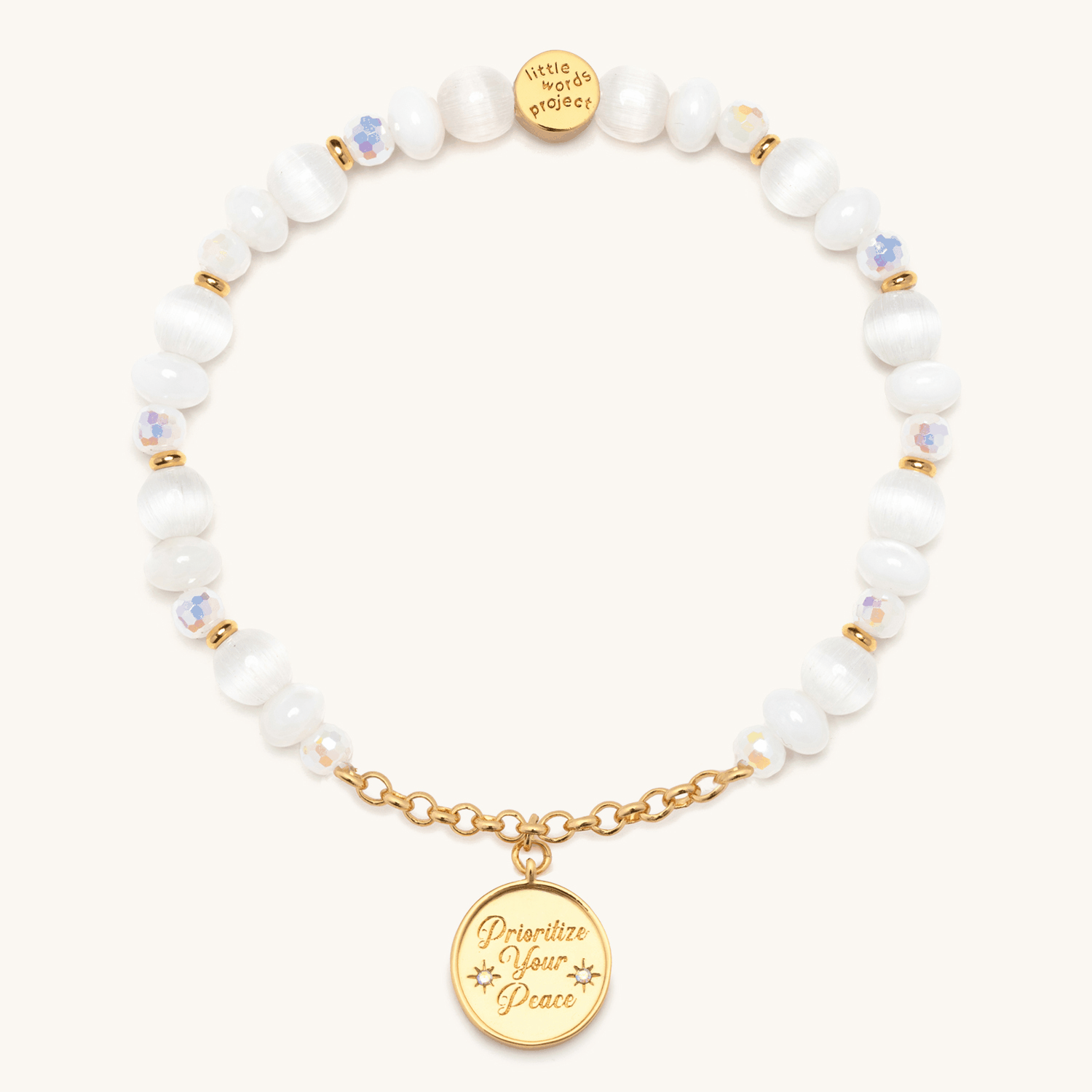 Prioritize Your Peace Charm Bracelet animation flipping the round gold medallion between the engraved Prioritize Your Peace front and the dove back, white cat eye and iridescent crystal beads, on cream background