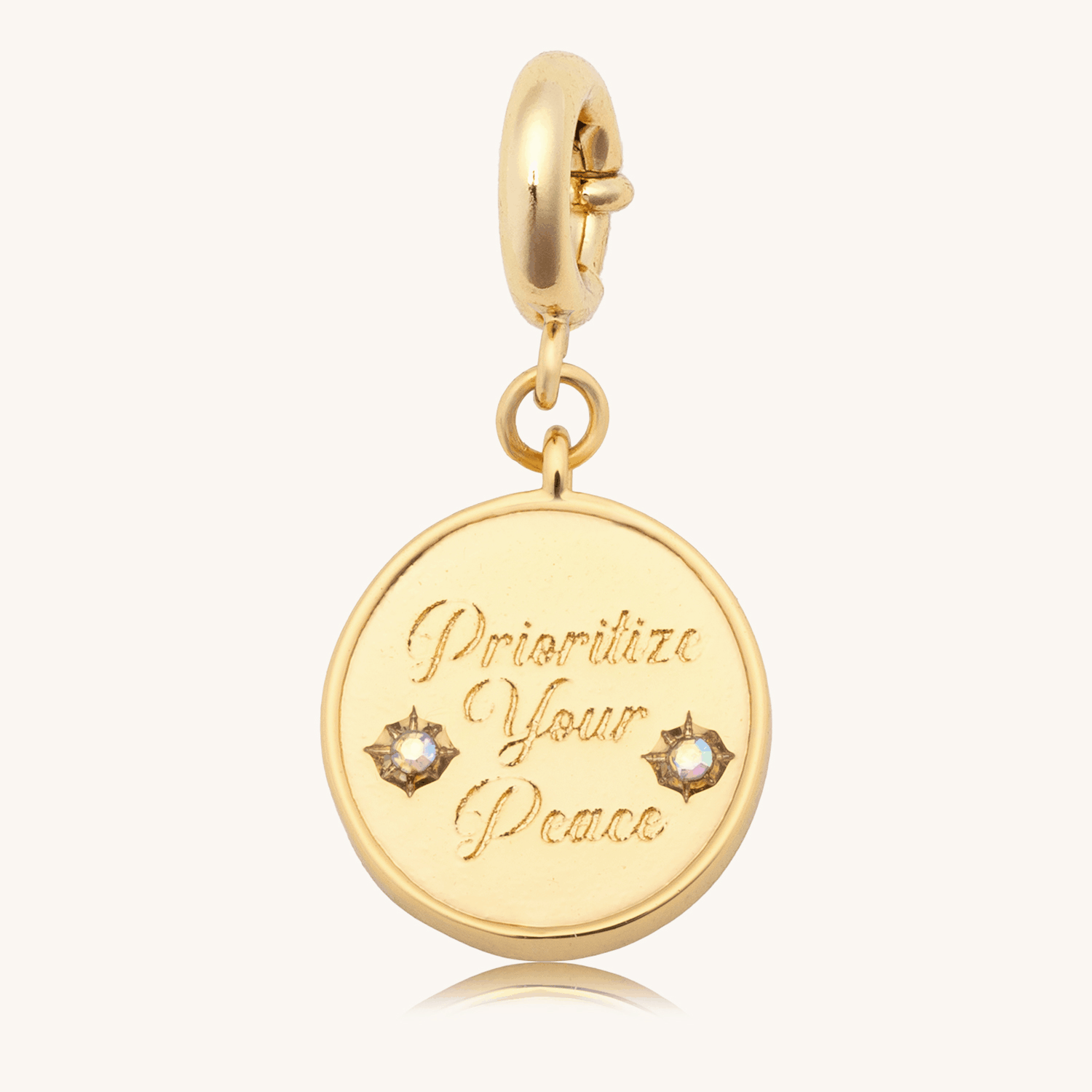 Prioritize Your Peace Charm animation flipping the 18k gold-plated round medallion between the engraved Prioritize Your Peace front with CZ starbursts and the dove back, on cream background
