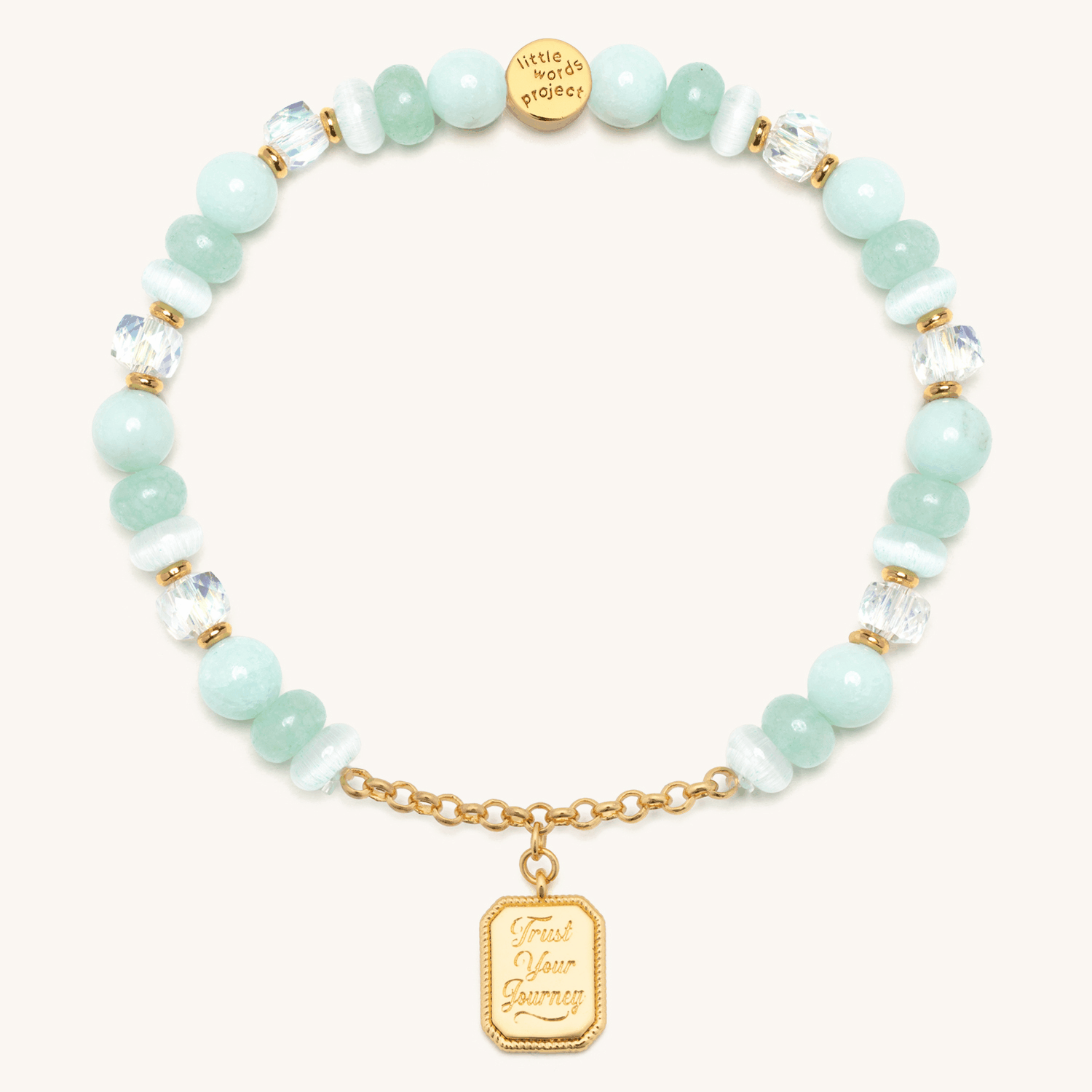 Trust Your Journey Charm Bracelet animation flipping the gold medallion between the engraved Trust Your Journey front and the CZ sun over a winding road back, seafoam and white cat eye beads, on cream background