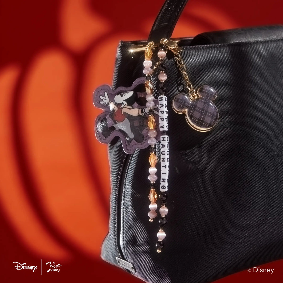 Happy Haunting Disney Mickey & Friends Bag Charm clipped to a black handbag, showing the vampire Mickey Mouse figure, plaid Mickey Mouse silhouette charm, and beaded Happy Haunting word strand
