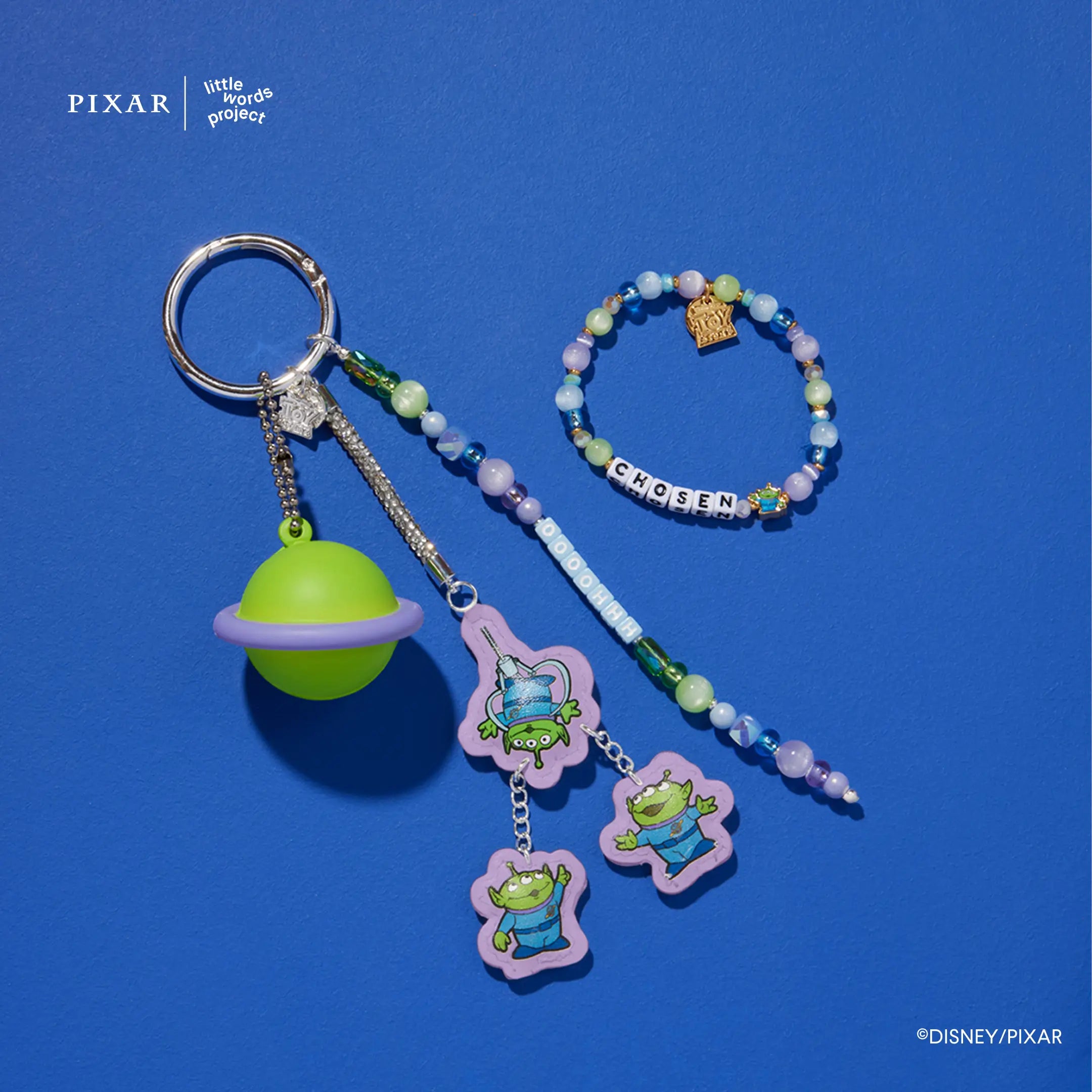 Oooohhhh Alien Set, Toy Story alien bag charm with green planet and alien charms plus the Chosen bracelet, flat lay on blue