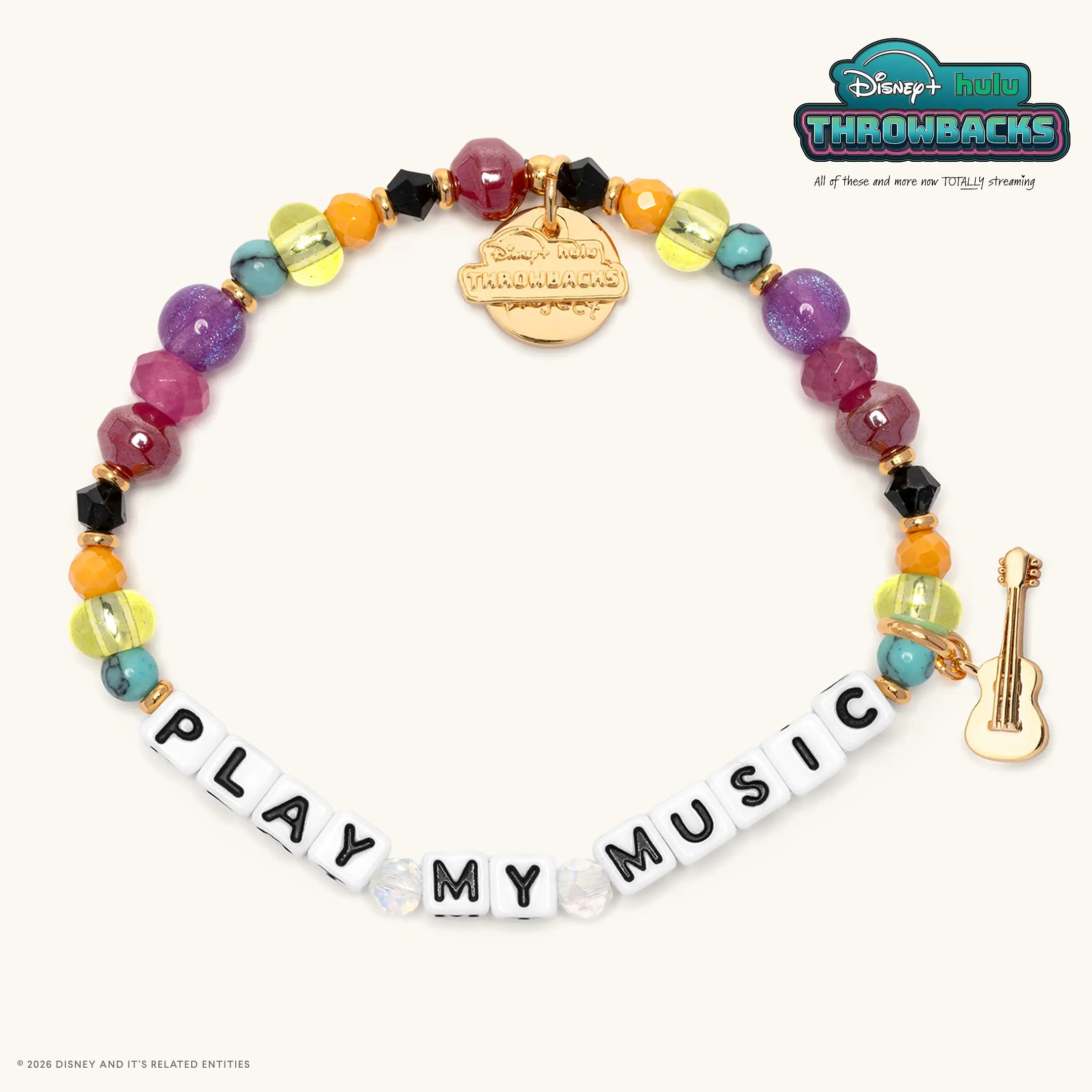 Play My Music Disney+ Hulu Throwbacks bracelet with rainbow beads in yellow, orange, turquoise, purple, and magenta, white letter beads, and a gold guitar charm, flat lay on cream