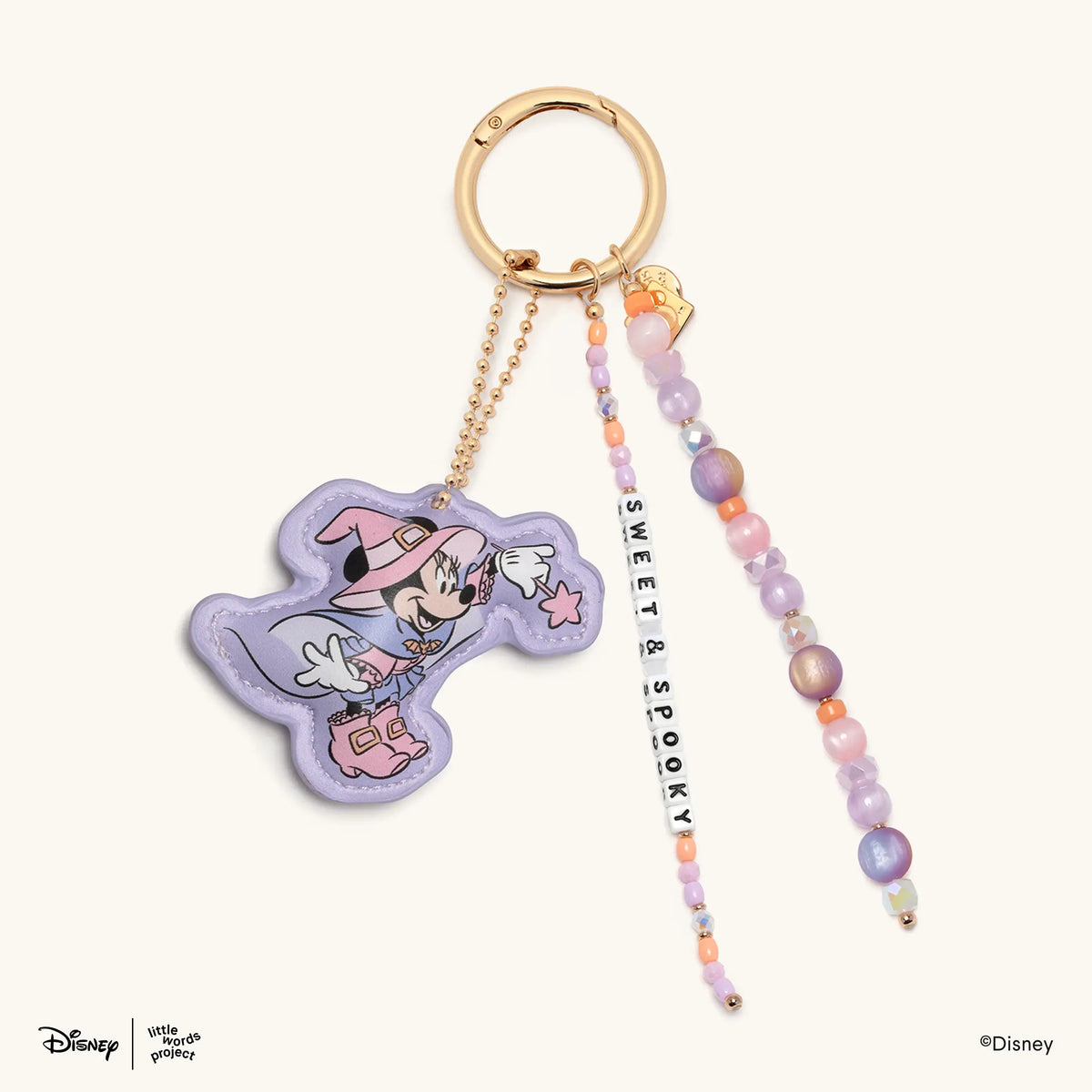 Sweet & Spooky Disney's Mickey & Friends beaded bag charm with a faux leather Minnie Mouse witch figure and lavender, pink, and orange beaded strands, flat-lay