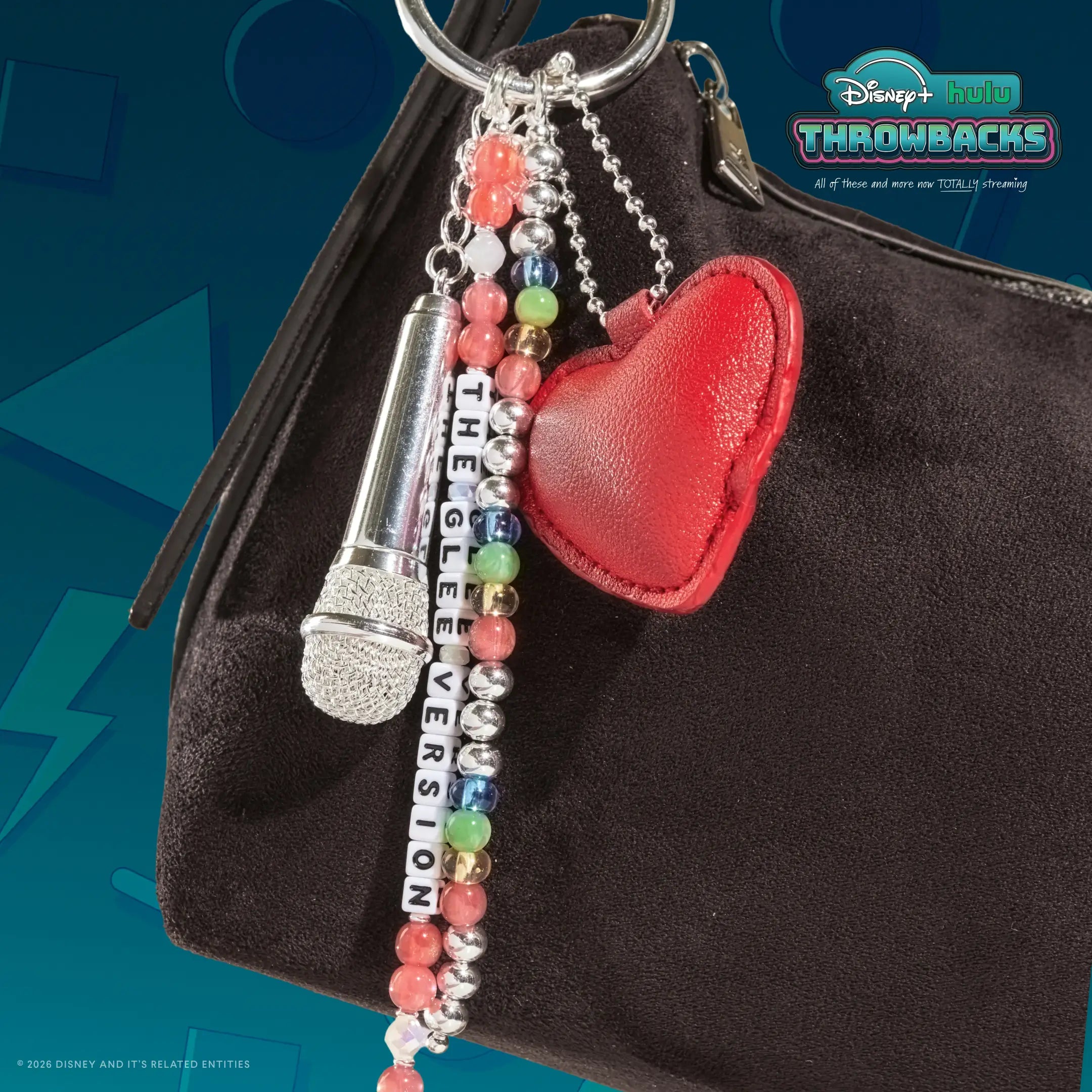 The Glee Version Disney+ Hulu Throwbacks bag charm clipped to a brown suede shoulder bag against a teal Y2K graphic backdrop