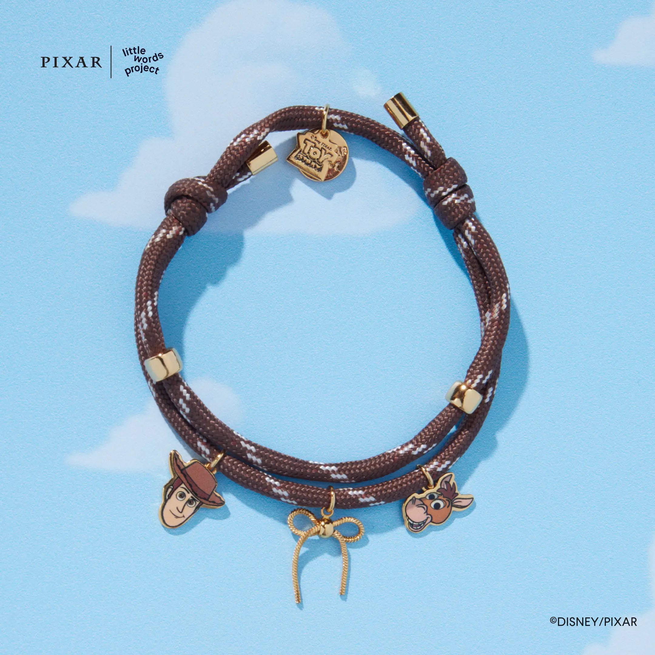 Woody's Round-Up brown corded Toy Story bracelet with gold charms on a blue sky background